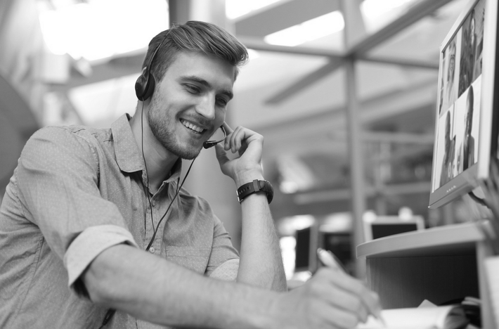 A man wearing headphones is sitting at a desk talking on a cell phone.