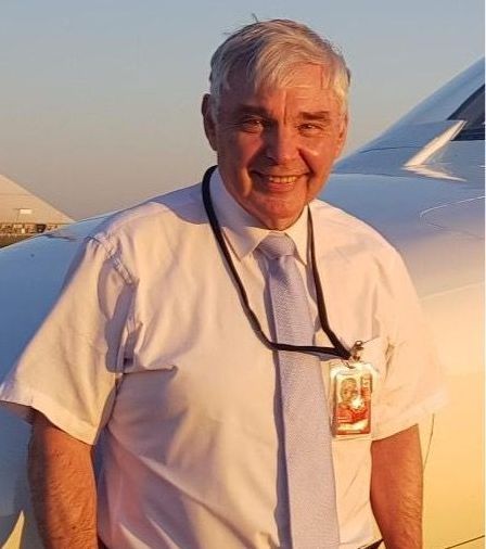 A man in a white shirt and tie is standing in front of an airplane.