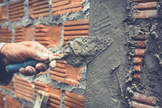 A man is plastering a brick wall with a trowel.