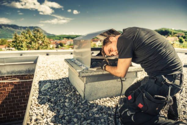 A man is kneeling down on a roof working on a chimney.