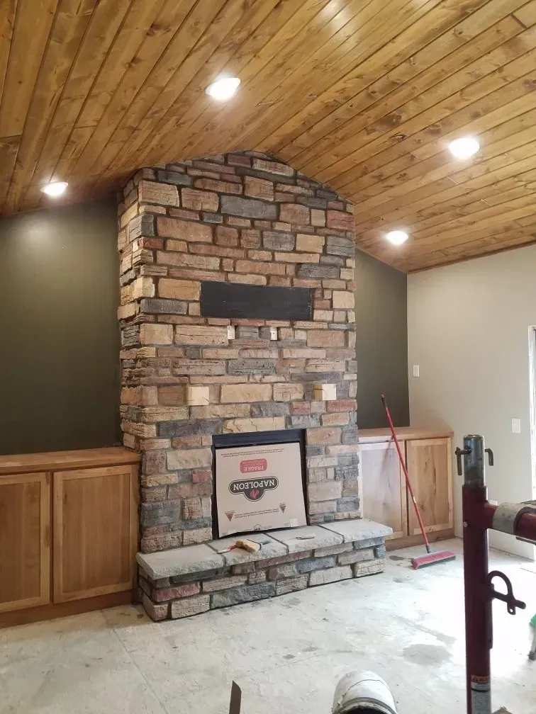 A living room with a stone fireplace and a wooden ceiling.