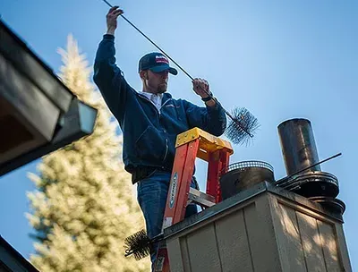 A man on a ladder is cleaning a chimney with a brush.