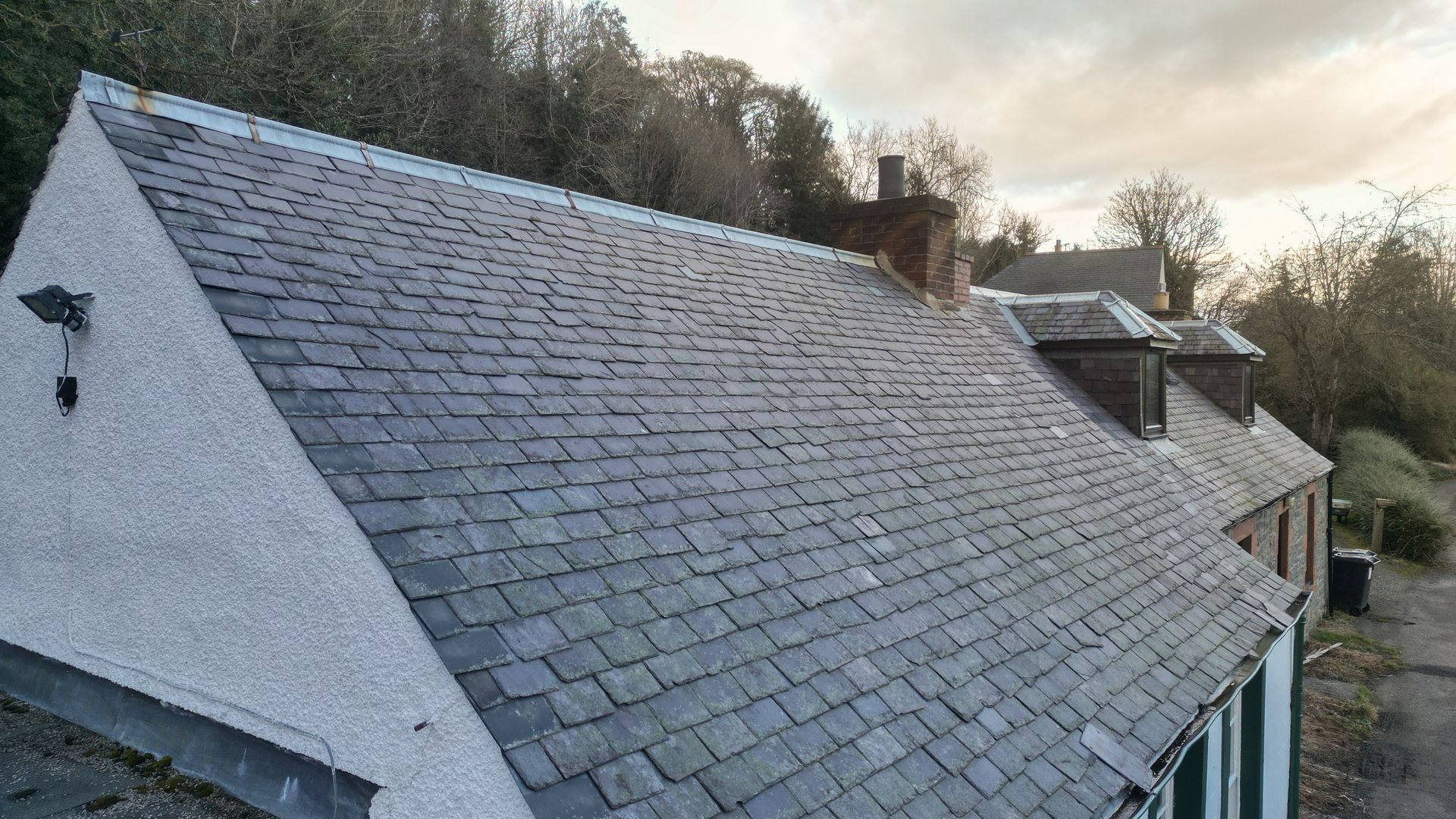 Slate roof peaks above trees under a clear, sunny sky.