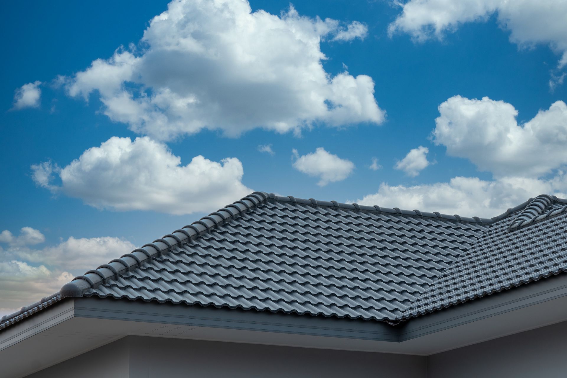 Gray tiled roof against a blue sky with fluffy white clouds.