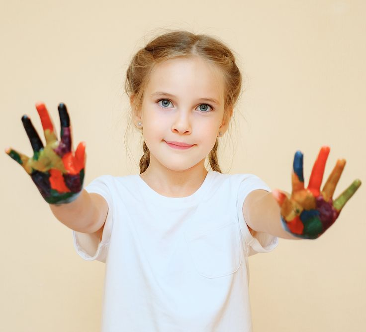 Ragazza con le mani ricoperte di vernice, sorride e tiene le mani verso l'osservatore.