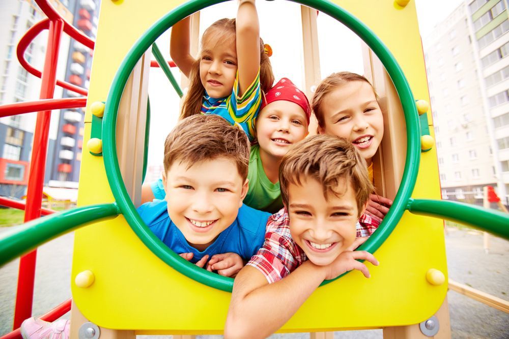 Bambini che sorridono e giocano insieme in un parco giochi colorato.