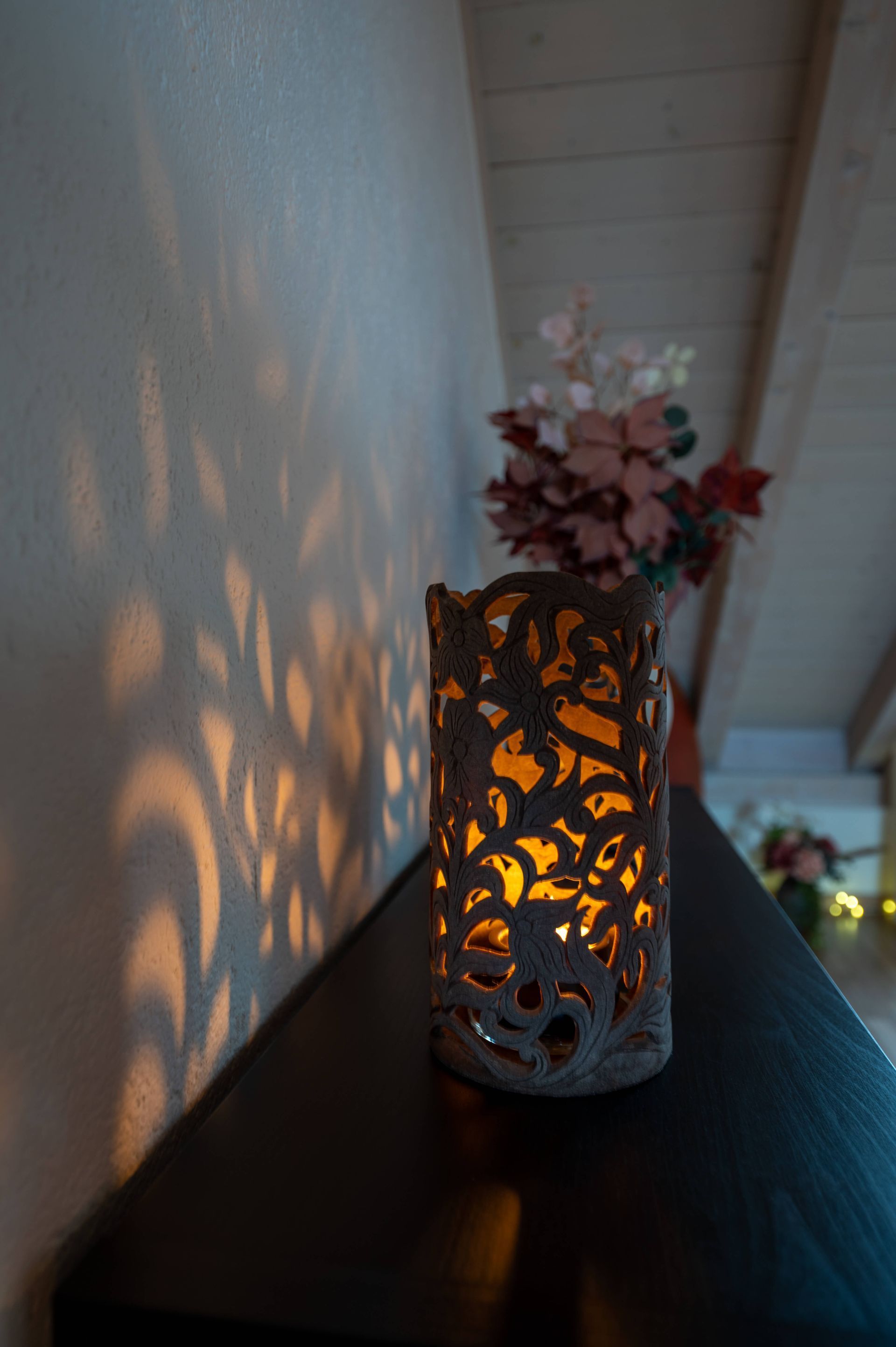 Eine leuchtende Lampe die Lichtmuster auf die Wand zaubert steht auf einer Kommode neben einer Vase mit Blumen.