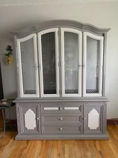 A gray and white hutch is sitting on a wooden floor in a living room.