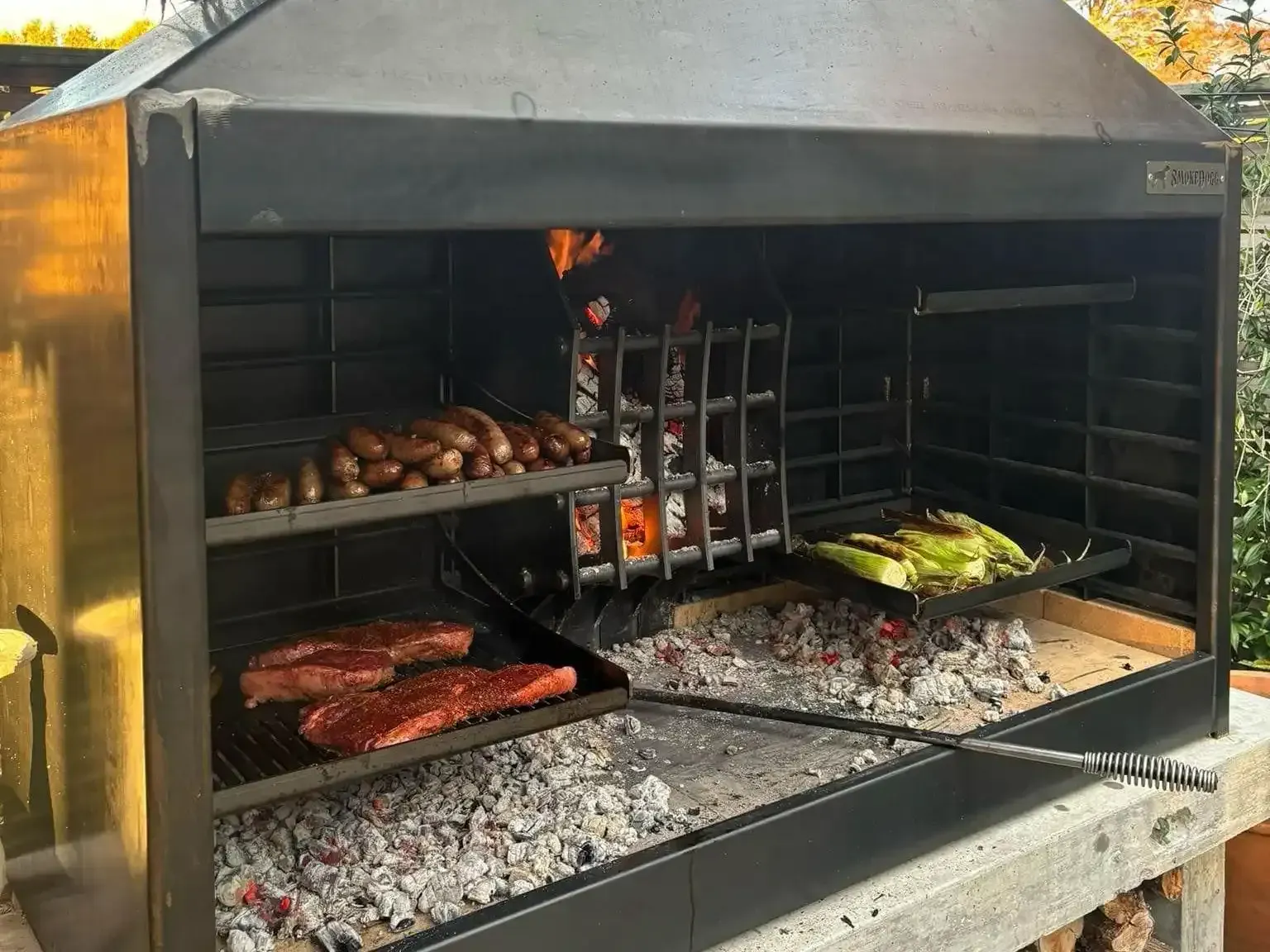 A large grill is sitting in the grass next to a pile of logs.