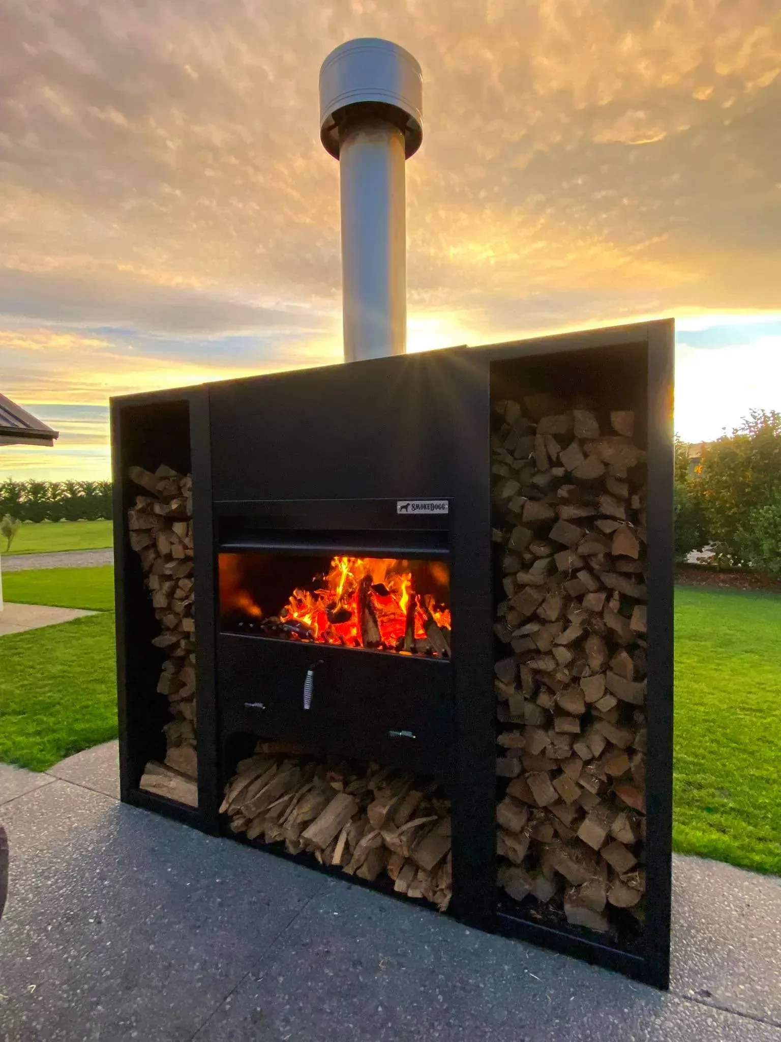 A large outdoor fireplace with a chimney and a pile of logs behind it.