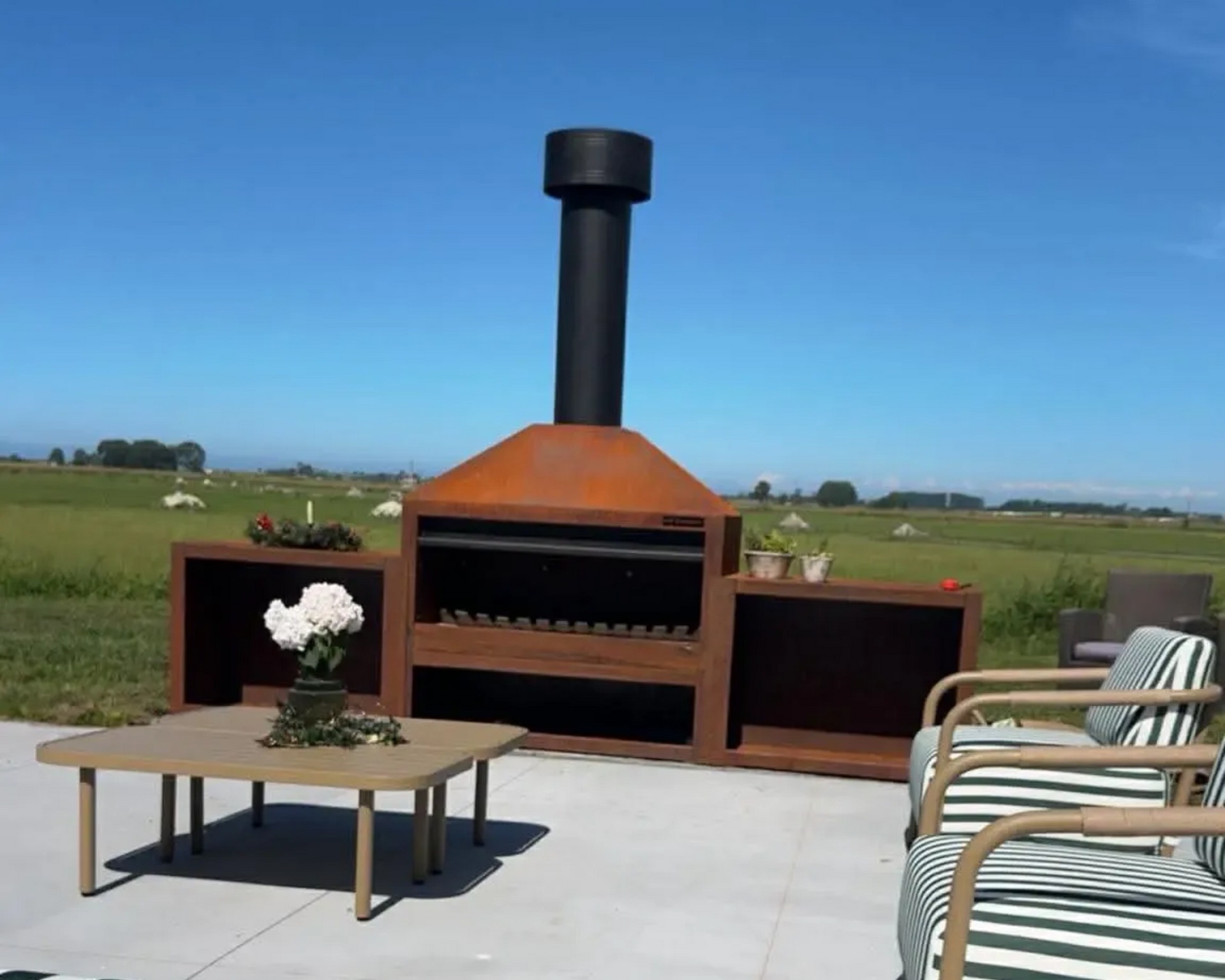 Outdoor barbecue with black chimney, side storage, table, and seating on a patio.