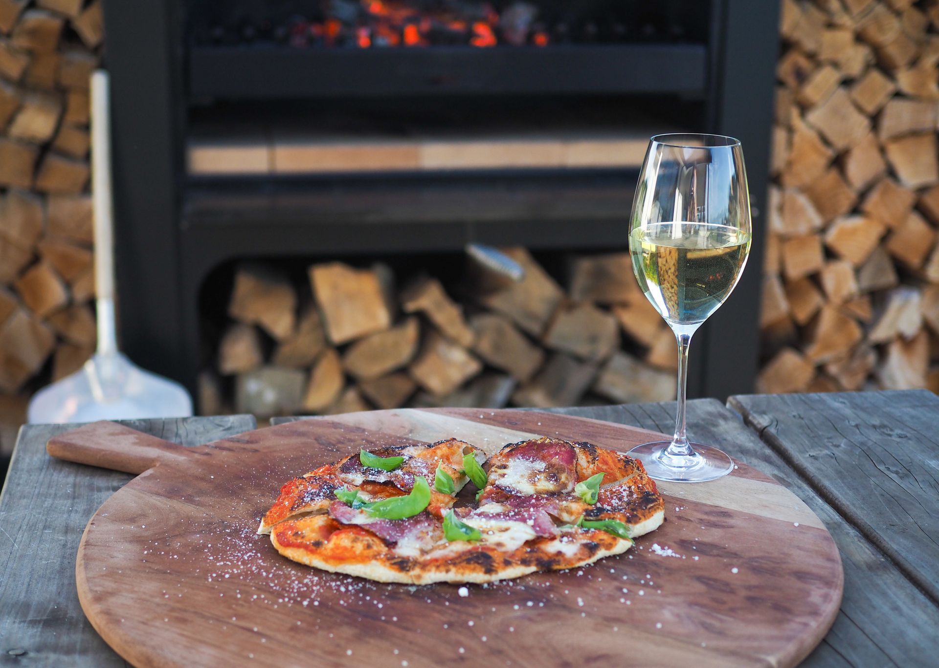 A pizza is sitting on a wooden cutting board next to a glass of wine.