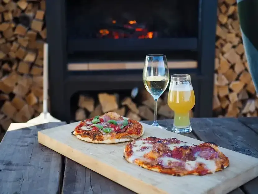 Two pizzas are sitting on a wooden cutting board next to a glass of wine.