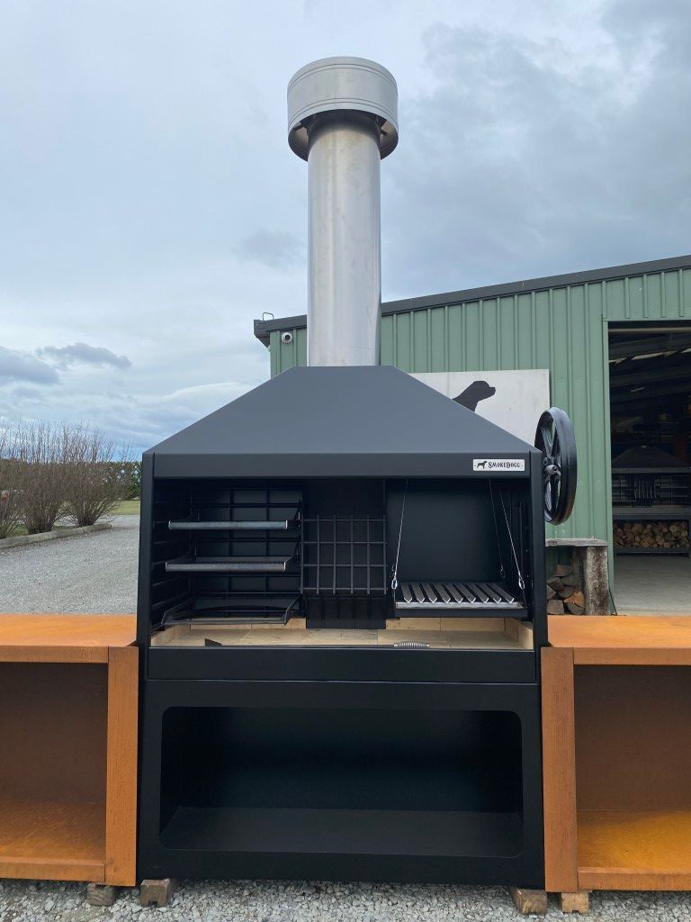 A large grill with a chimney on top of it is sitting in front of a building.