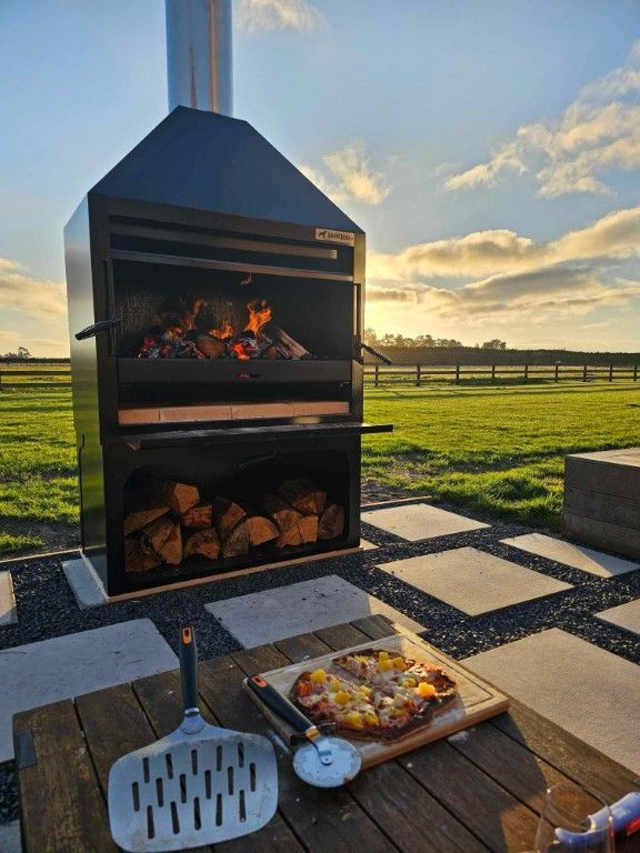 A pizza is sitting on a wooden table in front of a fire pit.