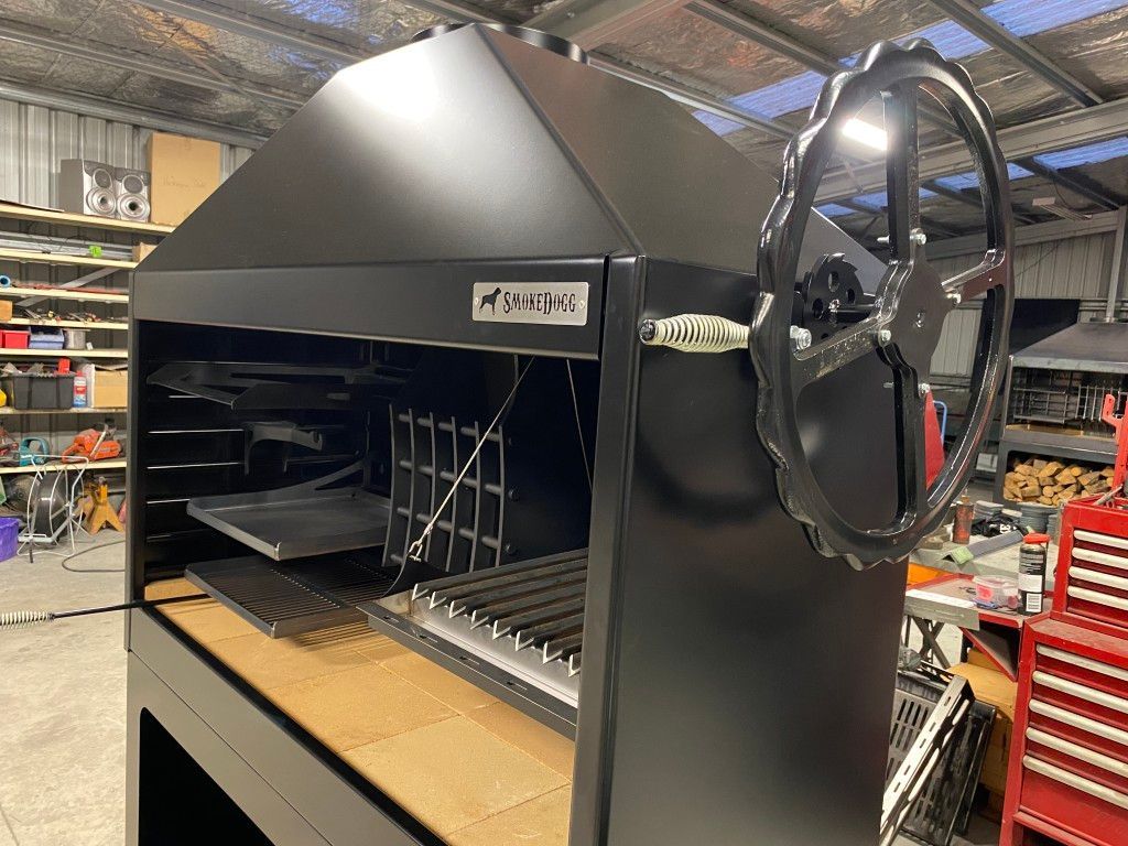 A black grill with a steering wheel attached to it is sitting on top of a wooden table.