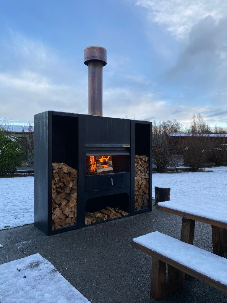 A large fireplace with a chimney is surrounded by snow and a picnic table.