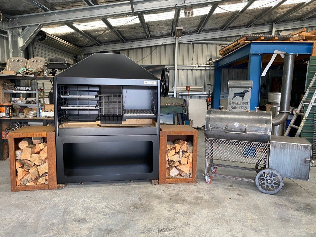A large bbq grill is sitting in a warehouse next to a wood rack.