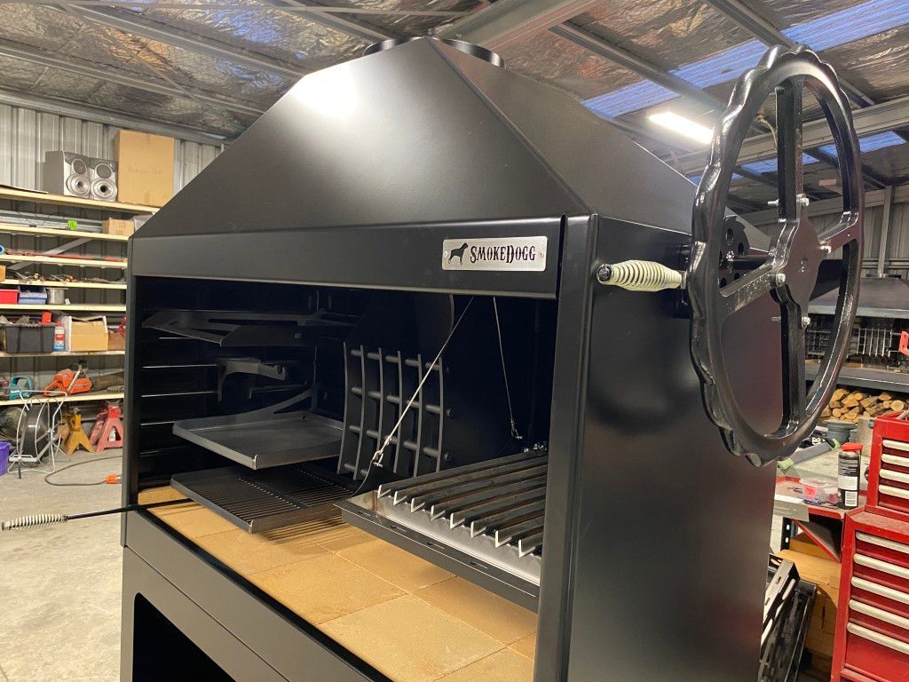 A large black grill is sitting on top of a wooden table in a warehouse.
