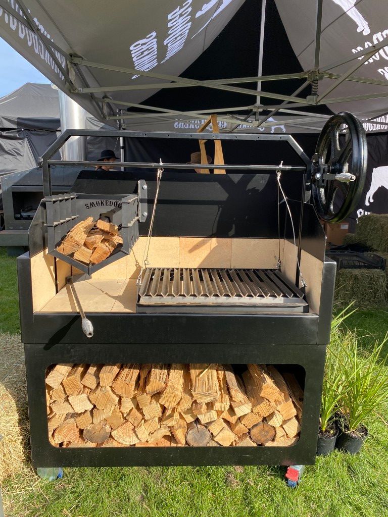A grill with a bunch of wood in it is sitting in the grass.