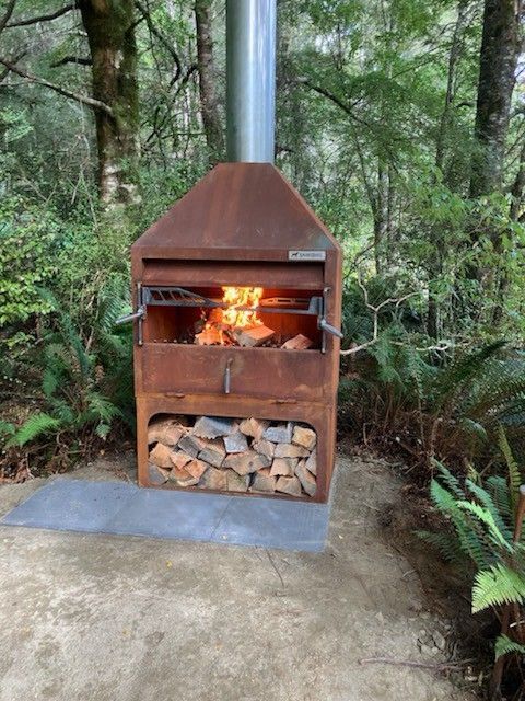 A fire place with a lot of wood in it is sitting in the middle of a forest.