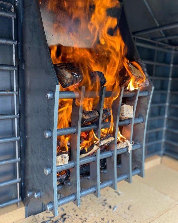 Fire burning in a metal wood-burning fireplace with a grate, set against a blue-tiled wall.
