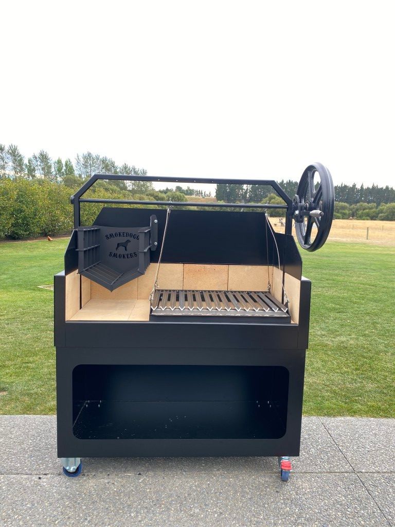 A large black grill is sitting on top of a concrete surface in front of a grassy field.