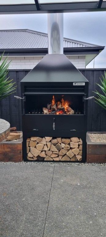 A wood stove is sitting on a patio next to a house.