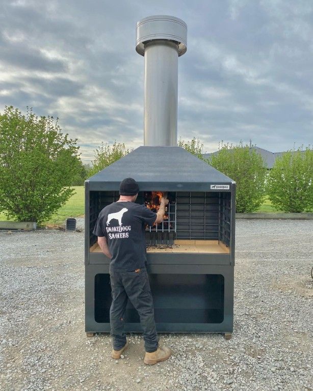 A man in a black shirt is standing in front of a large grill.