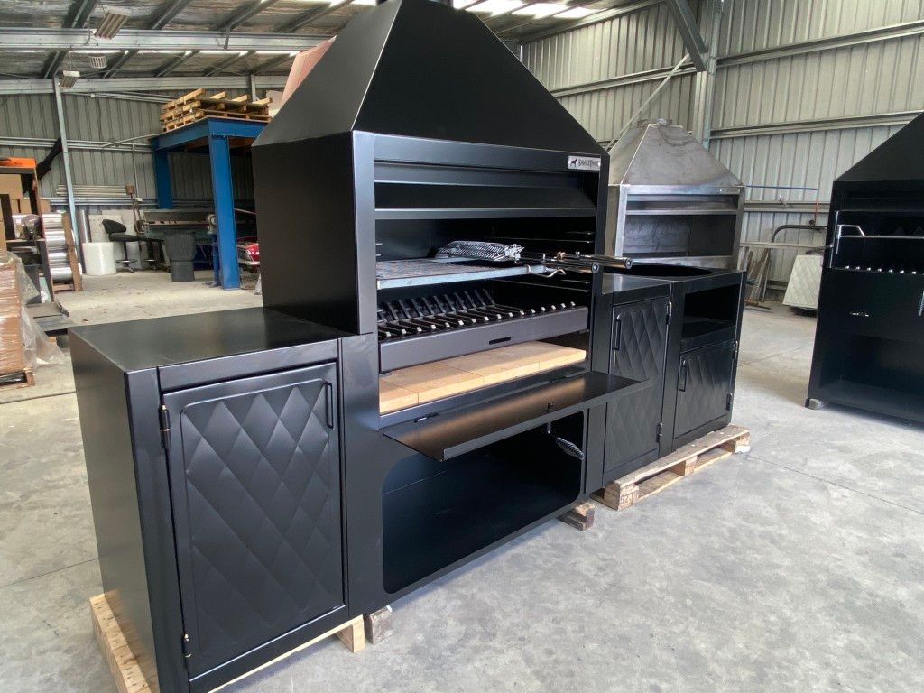 A large black grill is sitting in a warehouse with other grills.