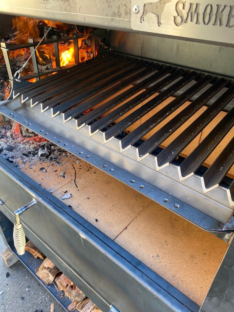 Large outdoor smoker with metal grates over a wood fire.