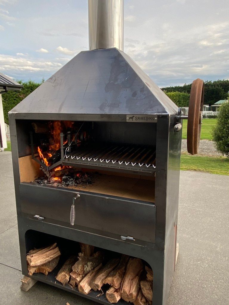 A large grill with a chimney on top of it is filled with wood.