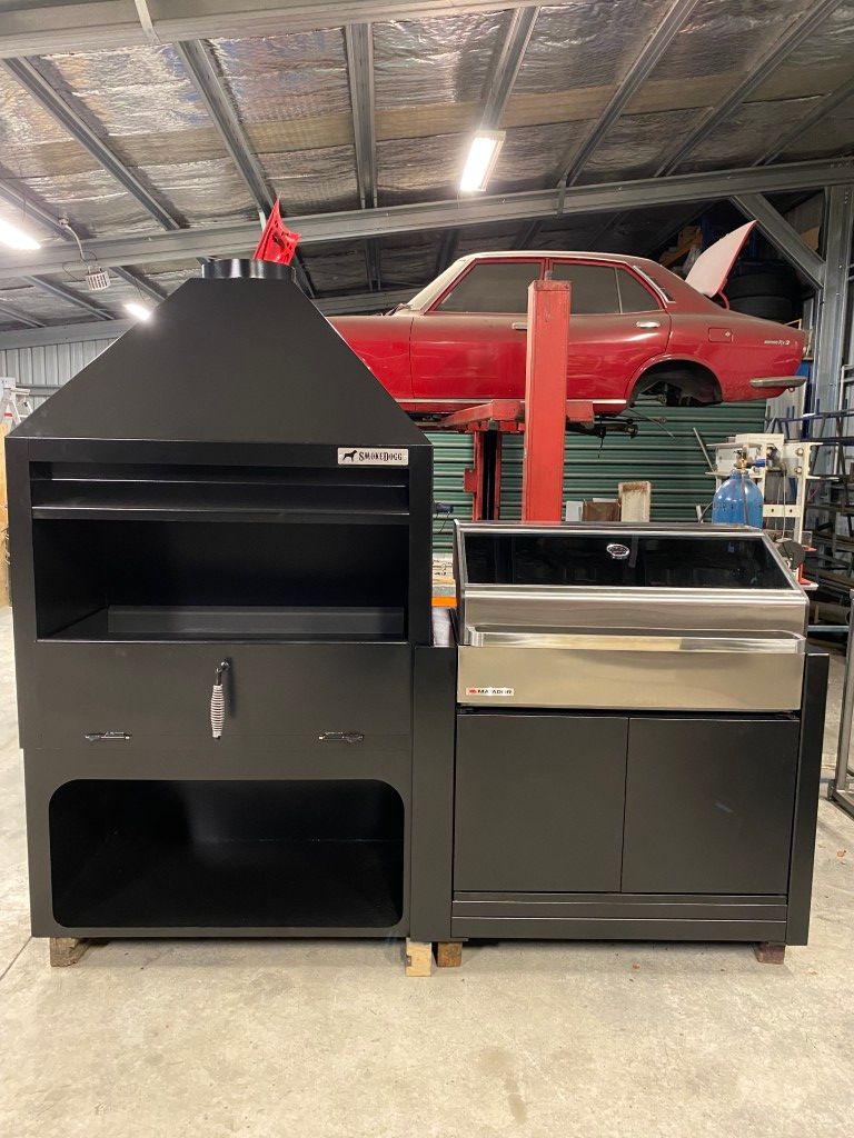 A red car is sitting on a lift in a garage next to a grill.