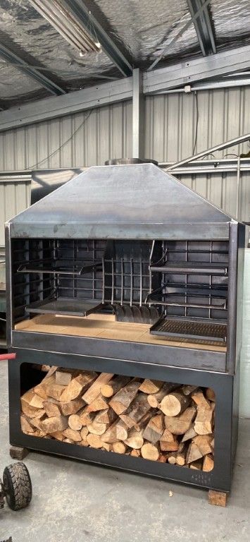 A large grill is sitting in a warehouse next to a pile of logs.