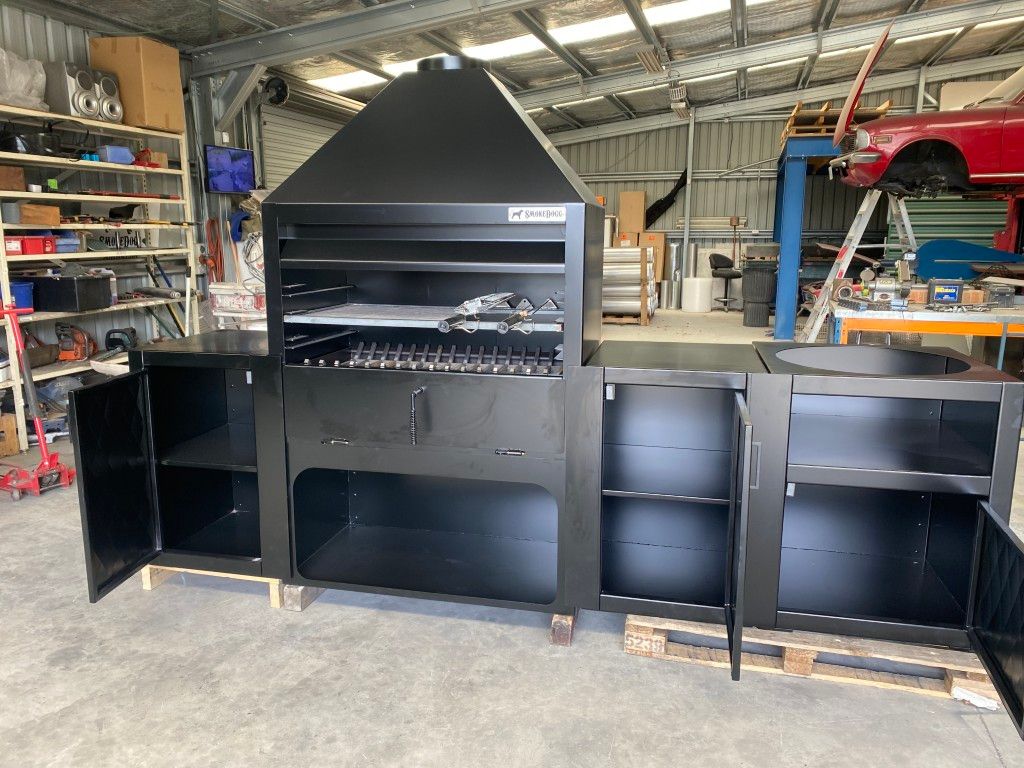 A large black grill is sitting in a warehouse with its doors open.