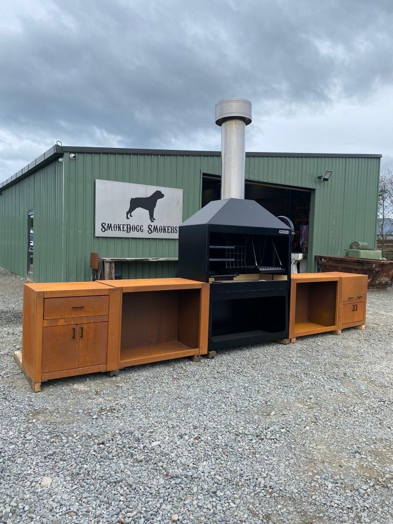A large grill is sitting in front of a green building.