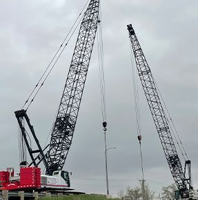 Two large cranes are sitting next to each other on a cloudy day.