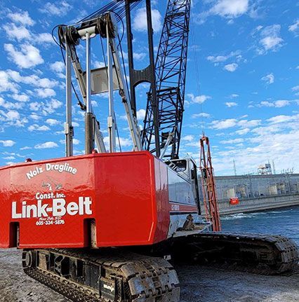 A red link belt crane is parked in front of a body of water.