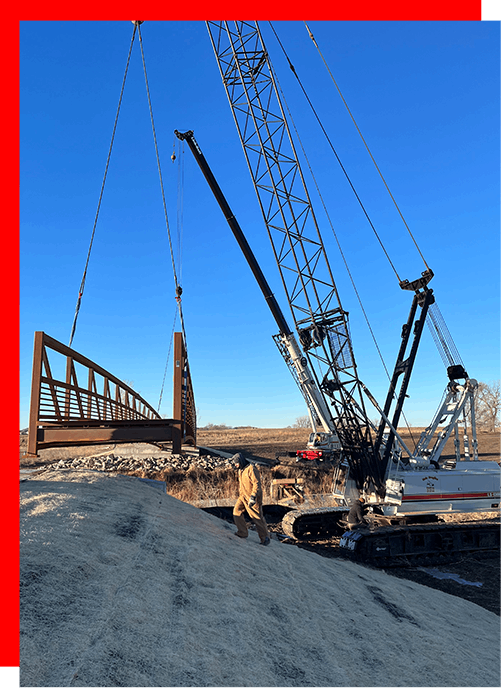 A man is standing in front of a large crane lifting a bridge