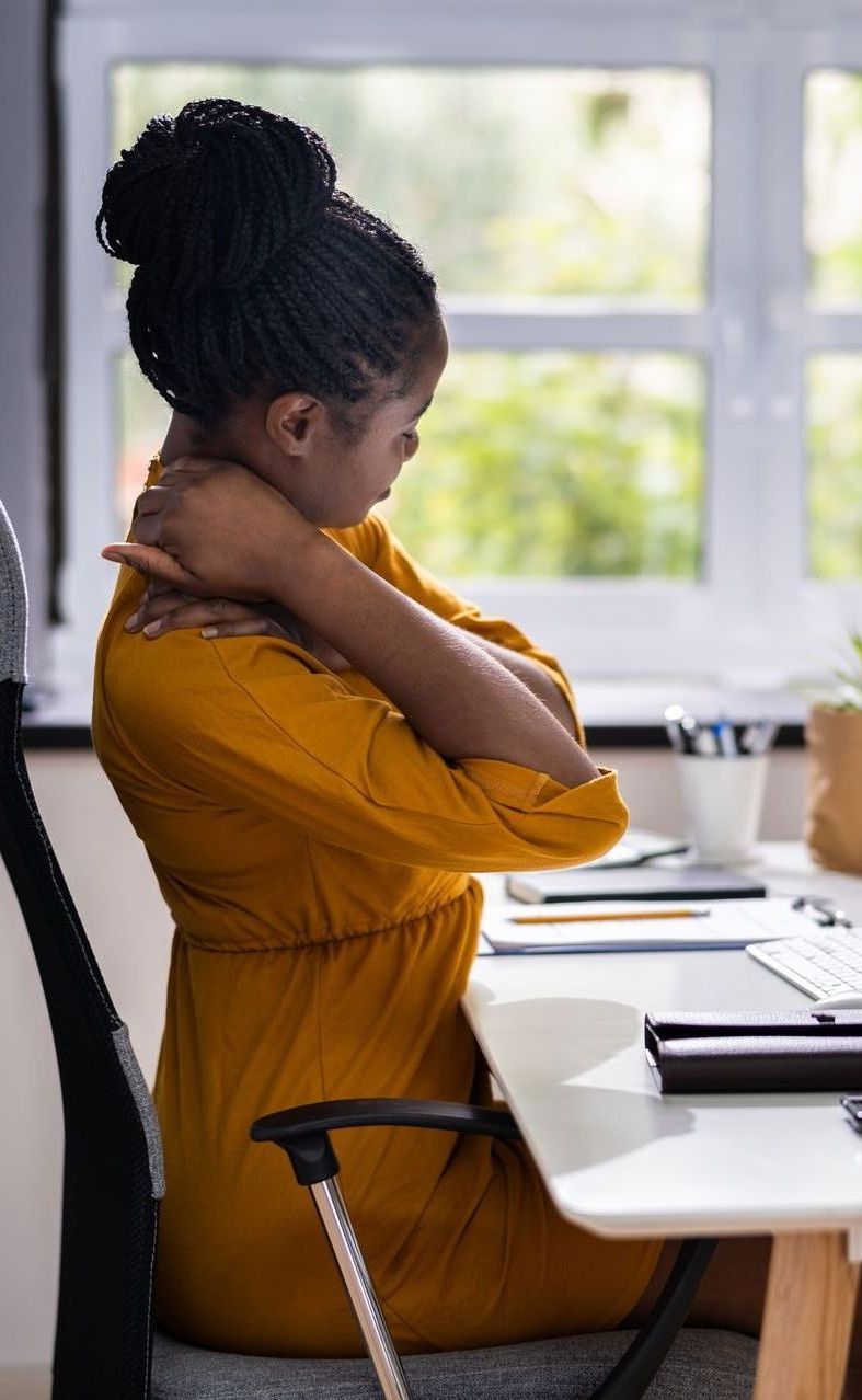 A woman is sitting at a desk holding her neck in pain.