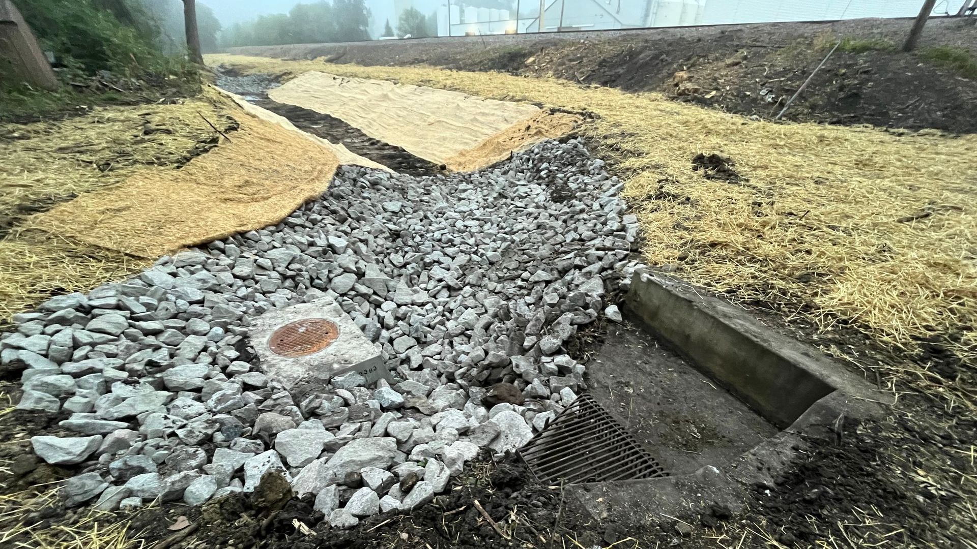 Drainage ditch with gravel, straw, and a concrete outlet.