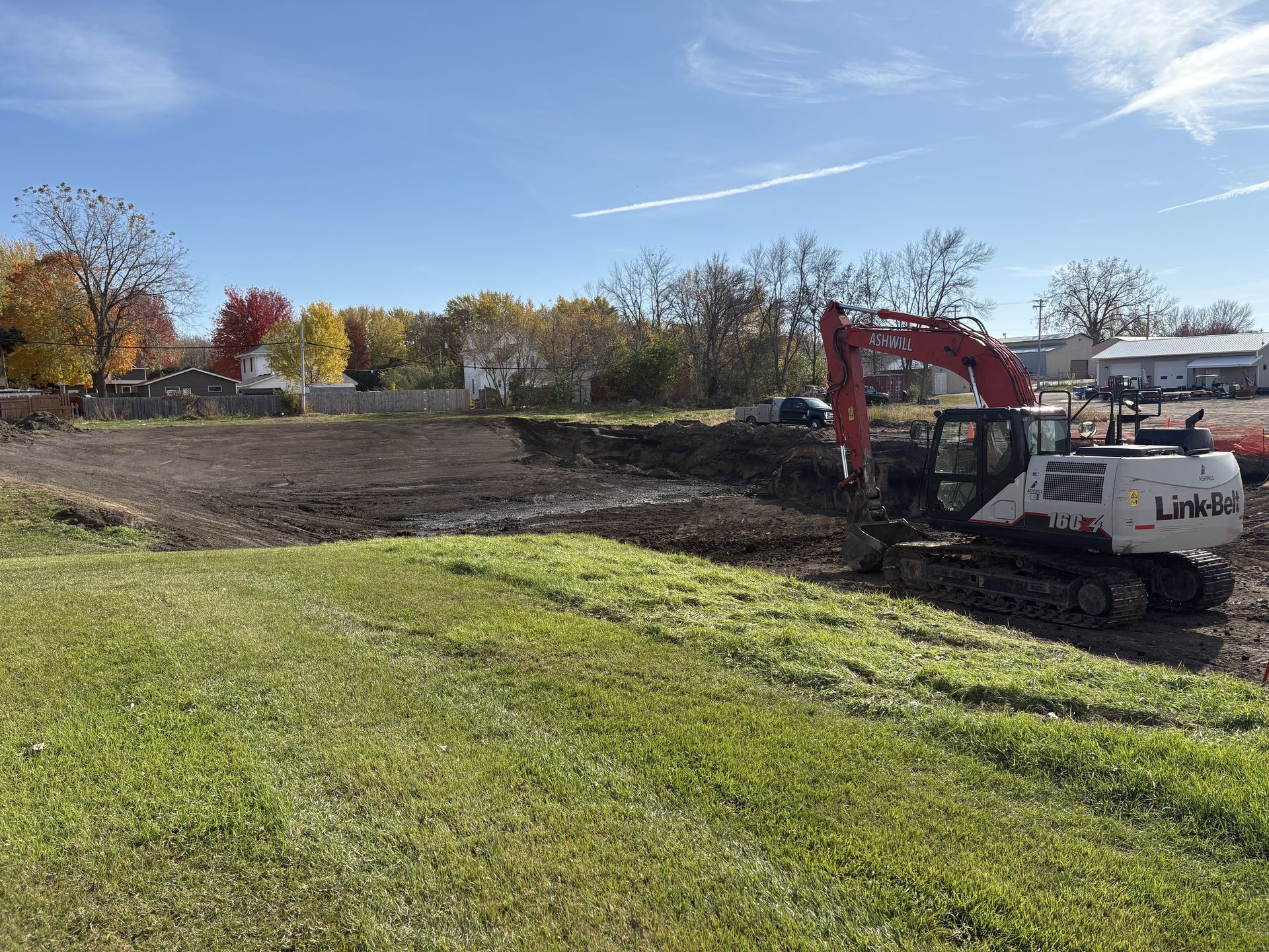 An excavator in a construction site, surrounded by dirt mounds, and surveying equipment. Overcast sky.
