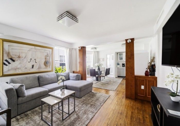 Bright living room with gray sectional, wood floors, large wall art, and a wall-mounted TV