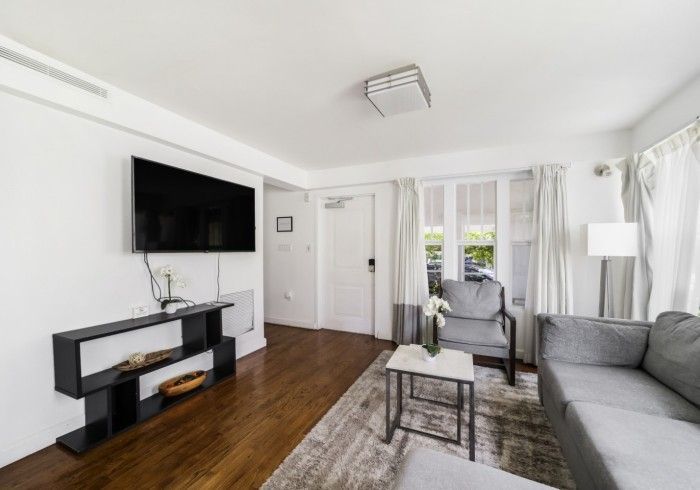 Bright living room with gray sofa, wall-mounted TV, wood floor, and large window.
