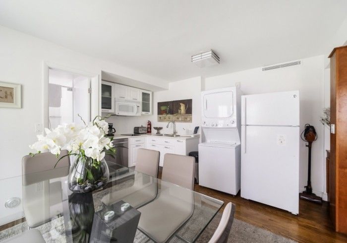 Bright kitchen with white appliances, glass dining table, and flowers in a sunlit apartment