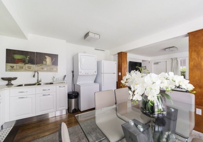 Bright modern kitchen and dining area with white cabinets, stainless appliances, and a glass table with white flowers