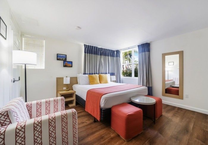 Modern hotel room with bed, red bench, armchair, and window with blue curtains