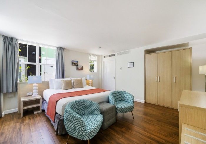 Bright bedroom with a bed, teal chairs, wooden floor, and a large wardrobe by a window.