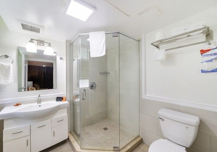 Bright white bathroom with vanity, mirror, glass shower, toilet, and wall-mounted towel bar.