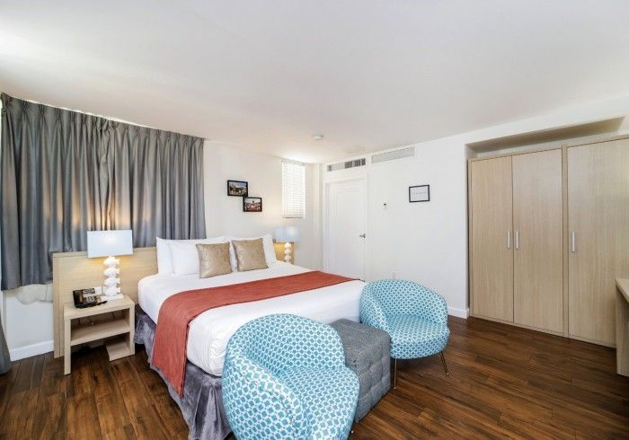 Bright bedroom with bed, blue chairs, lamp, curtains, and wardrobe on wood floor